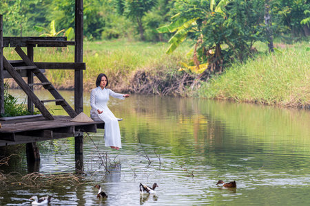 A Vietnamese girl in Vietnamese national costume is feeding fish.の写真素材