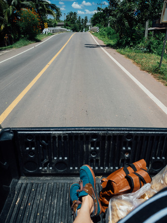 Man travel alone sit on truck bed, drive along the road surrounded by trees.