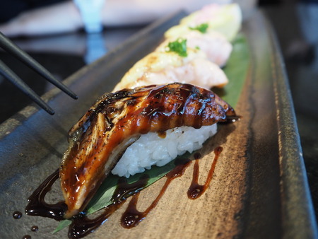 Closeup chopsticks going to grab grilled unagi sushi with teriyaki sauce and salmon sushi in background.の写真素材