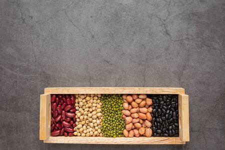 Grains or beans, red bean, black bean, green bean, soybean, peanut in the wooden tray placed on the black cement floor. Top view.の写真素材