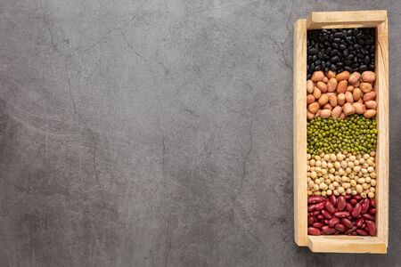 Grains or beans, red bean, black bean, green bean, soybean, peanut in the wooden tray placed on the black cement floor. Top view.の写真素材