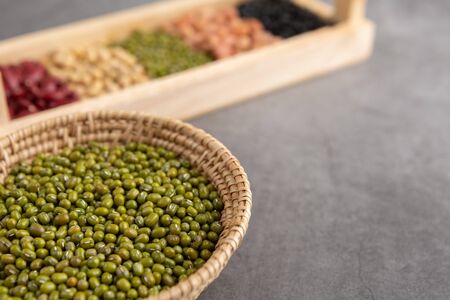 Green beans and grains in the wooden basket and in the wooden tray placed on the black cement floor....