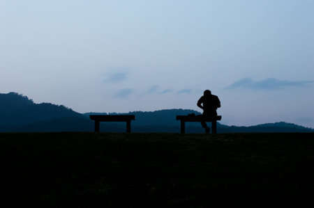 Silhouette of man sitting bench on top of the mountain view background.
