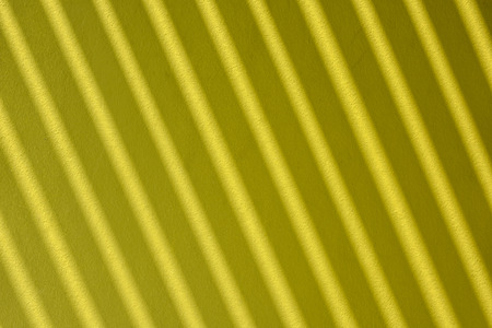 Diagonal shades of wooden screen on yellow green painted wallの写真素材