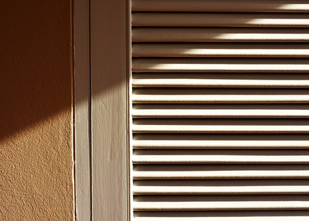 Sun shaded wooden door frame and panel painted white with light brown cement wall. Late afternoon...
