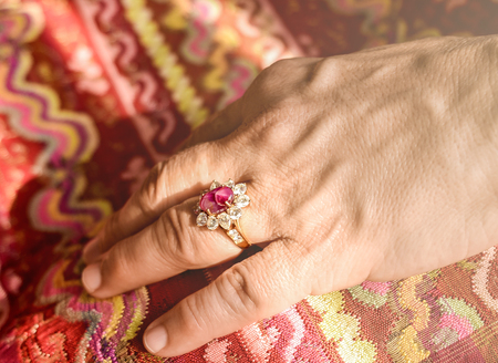 Mature Asian lady's hand wearing jewelry ring in one finger with traditional dress textile in background.Soft light effect added for vintage style.の写真素材