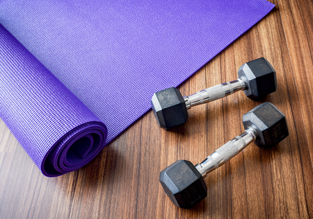 Working out equipment, two dumbbells and yoga mat on wooden floorの写真素材