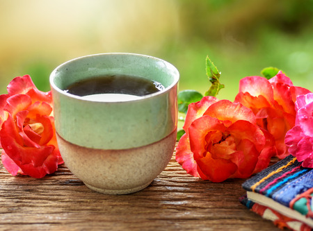 Hot tea in glazed ceramic cup with textile cover notebook and fresh orange roses from the garden. Tea time in the garden, soft light effect added with selective focus and shallow depth of field.の写真素材