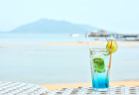 Cold refreshment drinks with blurry beach scenery background. Blue lagoon cocktail on the beachの写真素材