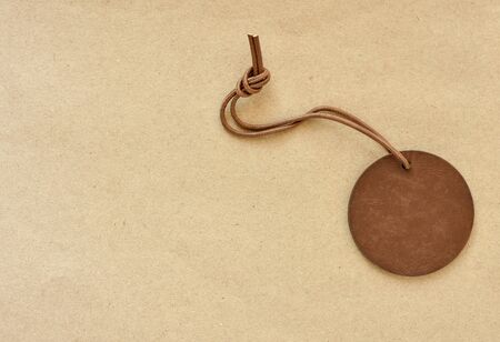 Blank round brown leather tag with leather cord on brown paper background.
