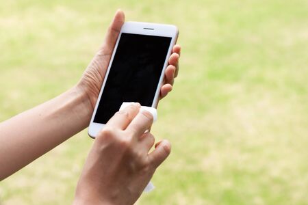 Thai woman wipes her hands with an alcohol towel washing mobile smartphone. Coronavirus prevention for hand hygiene corona virus protection. COVID-19 prevention sanitizing inside.の写真素材