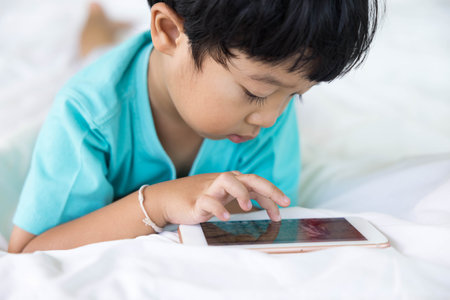 close up of happy boy Playing mobile, Taking pictures or selfie or video call or relatives in a bed. Concept of new generation, family, parenthood, authenticity, connectionの写真素材