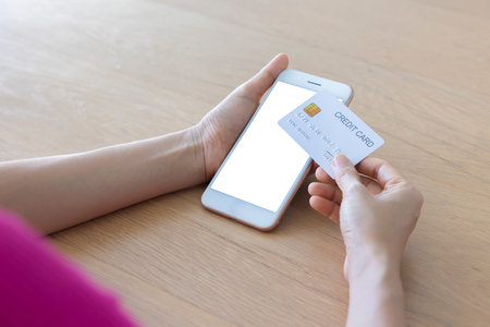 A woman shopping online on her table at home with a smartphone using a white credit card. And use your credit card to tap the screen to verify the identity. Concept about business. over shoulder shot.の写真素材