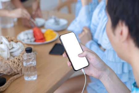 A man handled a smartphone with her left hand and using her right hand's finger to touch the white screen in a house. Concept about social, technology, business, modern, shopping. over shoulder shot.の写真素材