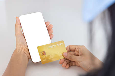 A woman shopping online on her sofa at home with a smartphone using a gold credit card. And use your...
