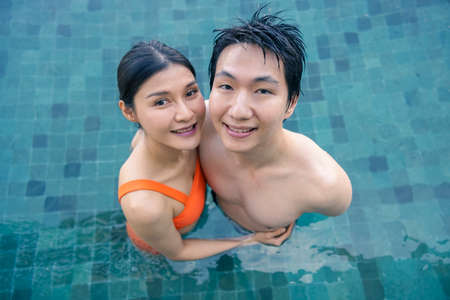 Woman and her boyfriend are happily cuddling in the outdoor swimming pool at the resort, the backdrop of the blue sea and sky. Wedding Hannimul trip of a couple. Concept of love, travel, happiness, nature.の写真素材