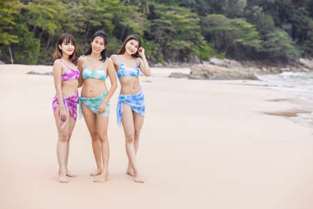 Three young women friends happily wear this bikini on a beach in Nai Thon Beach, Phuket Province, Thailand. Portrait of happy young woman smiling at sea. Concept about Travel, happiness, nature.の写真素材