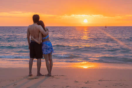 Young man and his girlfriend cuddle together on a beach with a sea back and a romantic sunset at Nai Thon Beach, Phuket, Thailand. Concept of summer holidays, vacation, travel, people.の写真素材