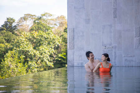 Woman and her boyfriend are happily cuddling in the outdoor swimming pool at the resort, the...