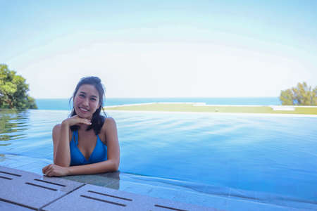 Portrait of beautiful young asian women, wearing blue bikini standing in the pool at resort looking...