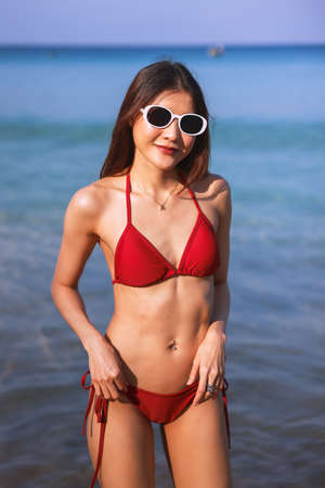 Vertical portrait of beautiful young asian women friends, wearing red bikini and stylish white...
