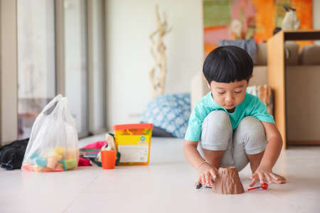 Cute little Asian boy plays with toy volcano happily on the floor of the children's room at home.
