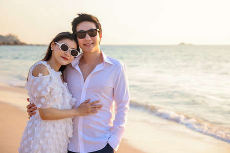 Young happy Asian couple hug on the beach, romantic travel honeymoon vacation summer holidays. Asian woman and man holding hands embracing outdoors.の写真素材