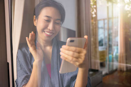 Portrait beautiful young asian woman is surfing the internet holding a phone in her hands at the bedroom. Concept home quarantine.の写真素材