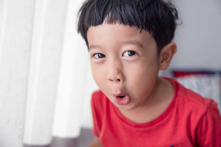 Close-up portrait Asian child boy straight black hair wearing a red shirt looking at camera of him make funny faces of happy smiling. Advertising childrens products.の写真素材