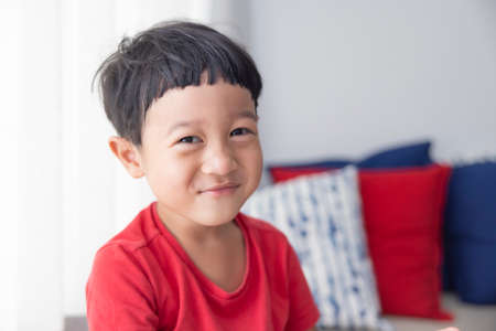 Close-up portrait Asian child boy straight black hair wearing a red shirt looking at camera of him make funny faces of happy smiling. Advertising childrens products.の写真素材