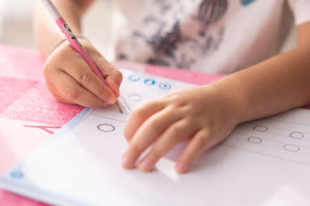 A boy's hand writes homework with a pink pencil on the table in his home's living room.の写真素材