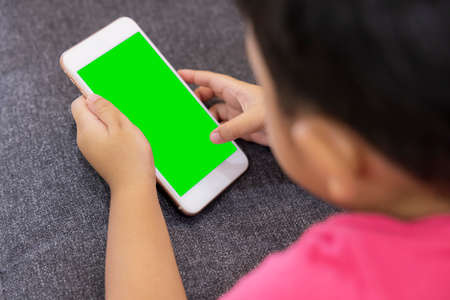 Smiling little boy looks at the touchpad lying on comfortable sofa in the living room. Enjoying playing game on digital smart phone green screen. Happy small kid using funny applications.の写真素材