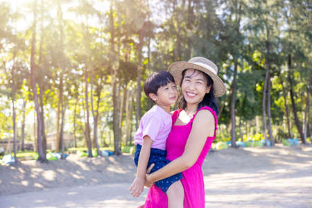 Asian boy and mom woman relaxing on tropical beach, they are njoy freedom and fresh air, wearing stylish hat and clothes. Happy smiling tourist in tropics in travel vacation.の写真素材