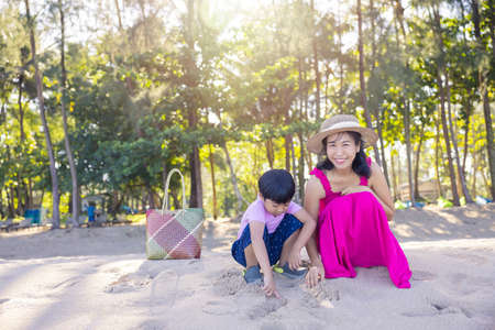 Asian boy and mom woman relaxing on tropical beach, they are njoy freedom and fresh air, wearing stylish hat and clothes. Happy smiling tourist in tropics in travel vacation.の写真素材