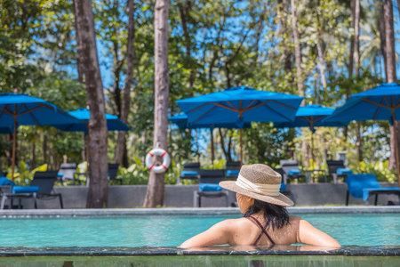 Happy asian woman in red swimsuit and a straw hat relaxing in swimming pool looking at view by the pool at Koh Mak, Phangnga, Thailand. relax and travel concept. Comfort resort summer vacation.の写真素材