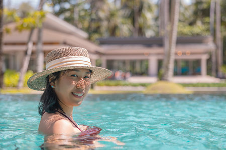 Happy asian woman in red swimsuit and a straw hat relaxing in swimming pool looking at camera by the pool at Koh Mak, Phangnga, Thailand. relax and travel concept. Comfort resort summer vacation.の写真素材