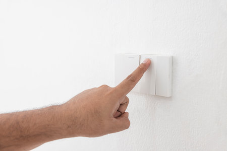 Close-up light switch of a male finger will turn on or off a light switch with white wall at home. white plastic mechanical switch mounted. Energy, energy, save electricity, copy space.の写真素材