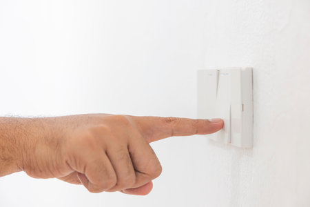 Close-up light switch of a male finger will turn on or off a light switch with white wall at home....