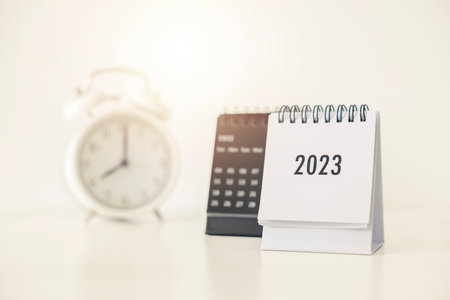 2023 business calendar and alarm clock on office table in new year day. Make a work plan for the...