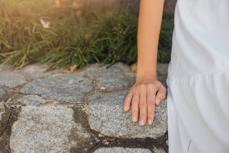 Close-up view, woman wearing white dress sitting on rock wall in resort educating, relaxing happily. concept about of relax, holiday, resort, comfort.の写真素材