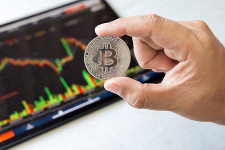 Close-up hand of man holding crypto coin on chart in tablet background. Blockchain technology finance future. Male hold bitcoin. concept about business, finance, trade, economy, banking, investment.の写真素材