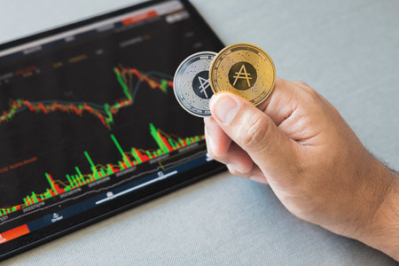 Close-up hand of man holding crypto coin on chart in tablet background. Blockchain technology finance future. Male hold ADA. concept about business, finance, trade, economy, banking, investment.の写真素材