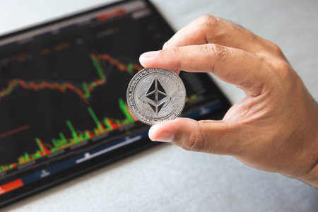 Close-up hand of man holding crypto coin on chart in tablet background. Blockchain technology finance future. Male hold Ethereum. concept about business, finance, trade, economy, banking, investment.の写真素材