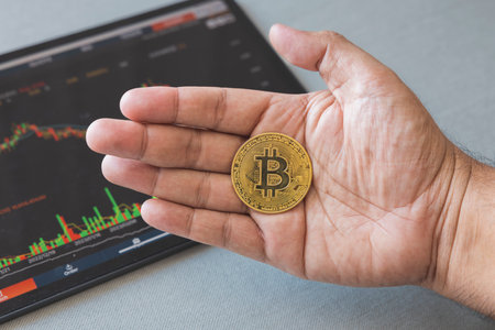 Close-up hand of man holding crypto coin on chart in tablet background. Blockchain technology...