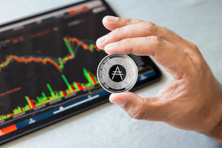 Close-up hand of man holding crypto coin on chart in tablet background. Blockchain technology finance future. Male hold ADA. concept about business, finance, trade, economy, banking, investment.の写真素材