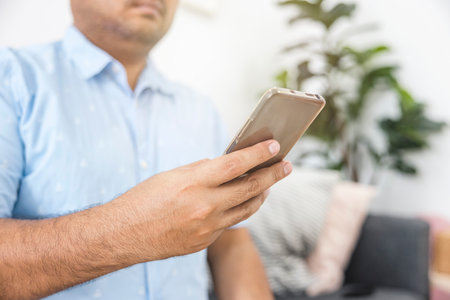 Asian man in blue shirt sitting on sofa in living room using smartphone. Holiday relaxation. Online shopping. Modern communication technology. about technology, rest, shop, relax.の写真素材