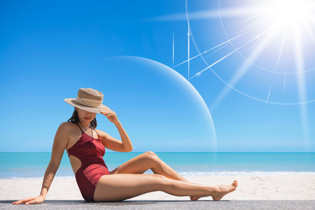 Asian model wear red swimsuit and straw hat sit on beach look view on hot day, Sun and UV rays hit the beautiful woman's protective layer. concept about of spa, sunscreen, cosmetics, health.の写真素材