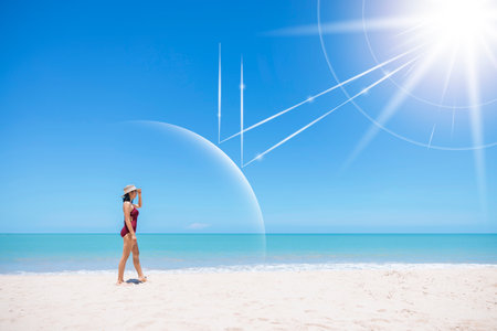 Asian model wear red swimsuit and straw hat walk on beach look view on hot day, Sun and UV rays hit the beautiful woman's protective layer. concept about of spa, sunscreen, cosmetics, health.の写真素材