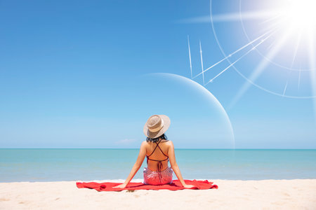 Asian model wear red swimsuit and straw hat sit on beach look view on hot day, Sun and UV rays hit the beautiful woman's protective layer. concept about of spa, sunscreen, cosmetics, health.の写真素材