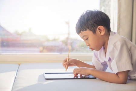 Happy Asian boy 6-7 years old, black hair, white skin, wearing white shirt and blue shorts writing on a chalkboard. Children in school uniforms of Thailand. concept about education, play, creativity.の写真素材